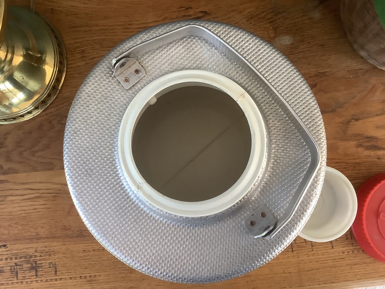 May include: A silver metal beverage cooler with a white lid and a handle. The cooler has a textured surface and a round opening.