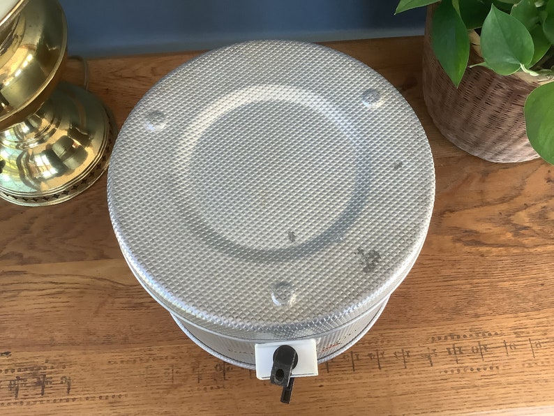 May include: A silver metal beverage dispenser with a textured surface and a black spigot. The dispenser is on a wooden surface.