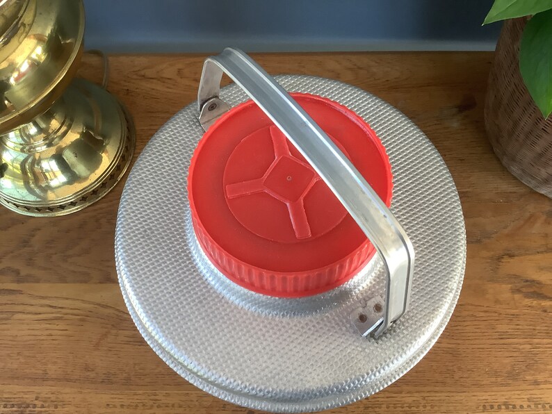 May include: A silver metal container with a red lid and a silver handle. The container has a textured surface.