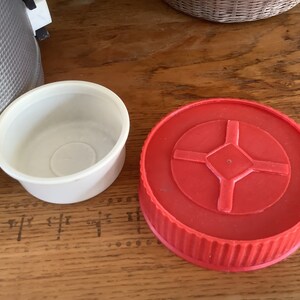 May include: Two round lids for a thermos or container. One lid is white and the other is red with a cross-shaped design in the center.