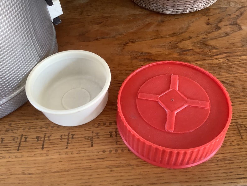 May include: Two round lids for a thermos or container. One lid is white and the other is red with a cross-shaped design in the center.