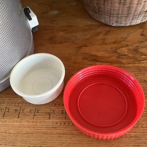 May include: Two plastic lids, one white and one red, are on a wooden surface. The white lid is smaller than the red lid.