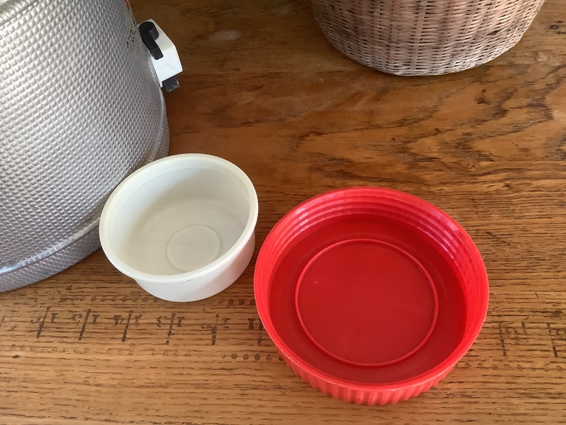 May include: Two plastic lids, one white and one red, are on a wooden surface. The white lid is smaller than the red lid.