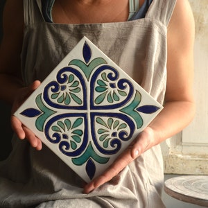 Peut inclure: Un carreau de céramique peint à la main avec un motif floral bleu et vert. Le carreau est carré et a un fond blanc.