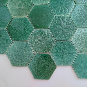 Op de afbeelding: Een verzameling turquoise zeshoekige tegels met reliëf bloemen- en geometrische patronen. De tegels zijn gerangschikt in een honingraatpatroon, met een verscheidenheid aan ontwerpen en texturen. De tegels hebben een effen turquoise kleur.