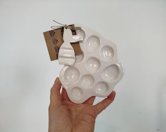 May include: White ceramic paint palette with 10 individual wells, shaped like a flower. A small ceramic rabbit figurine is attached to the palette.
