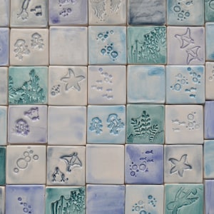 May include: A grid of square ceramic tiles featuring embossed ocean-themed designs in shades of blue, teal, and white. The tiles display various marine life including starfish, stingrays, jellyfish, coral, seaweed, and bubbles in a glossy finish.