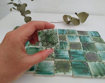 May include: A collection of green and white ceramic tiles with a decorative pattern. The tiles are arranged in a grid pattern and have a slightly textured surface.