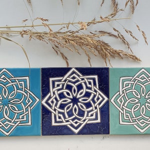 Può includere: Tre piastrelle in ceramica con un design geometrico bianco su sfondo blu, blu navy e verde.