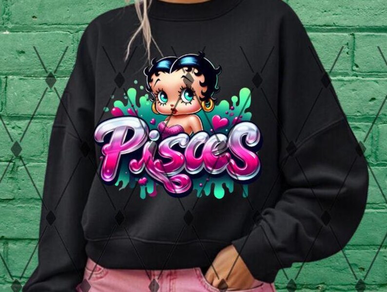May include: Black sweatshirt featuring a pink and green graphic of a cartoon character with the word "Pisces" in pink and green lettering.