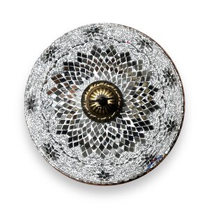 May include: A round, silver-toned decorative plate with a mosaic design. The plate has a central brass knob with a floral pattern.