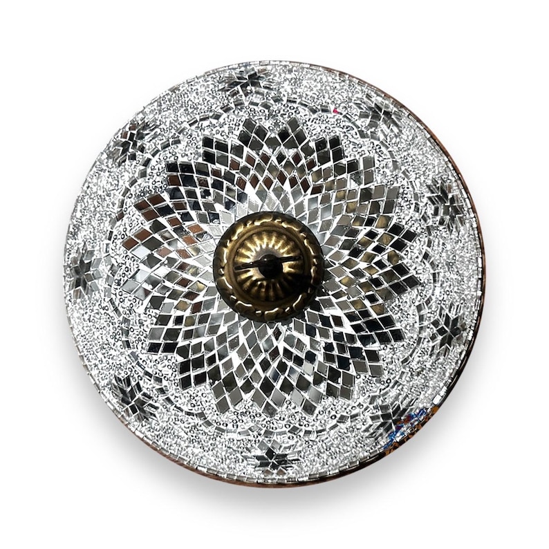 May include: A round, silver-toned decorative plate with a mosaic design. The plate has a central brass knob with a floral pattern.