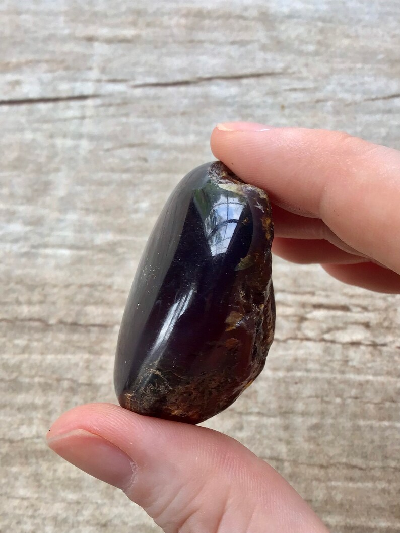 May include: A dark amber stone with a smooth, polished surface. The stone has a deep, rich color and a slightly translucent quality.
