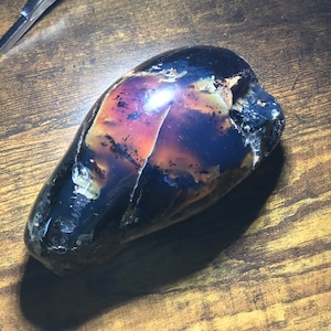 May include: A large, dark, purple, and black agate stone with a smooth, polished surface. The stone has a unique, natural pattern and is shaped like an egg.