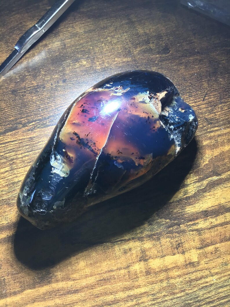 May include: A large, dark, purple, and black agate stone with a smooth, polished surface. The stone has a unique, natural pattern and is shaped like an egg.