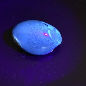 May include: A smooth, blue, oval-shaped stone with a white swirl pattern. The stone is illuminated with a bright, pink light.