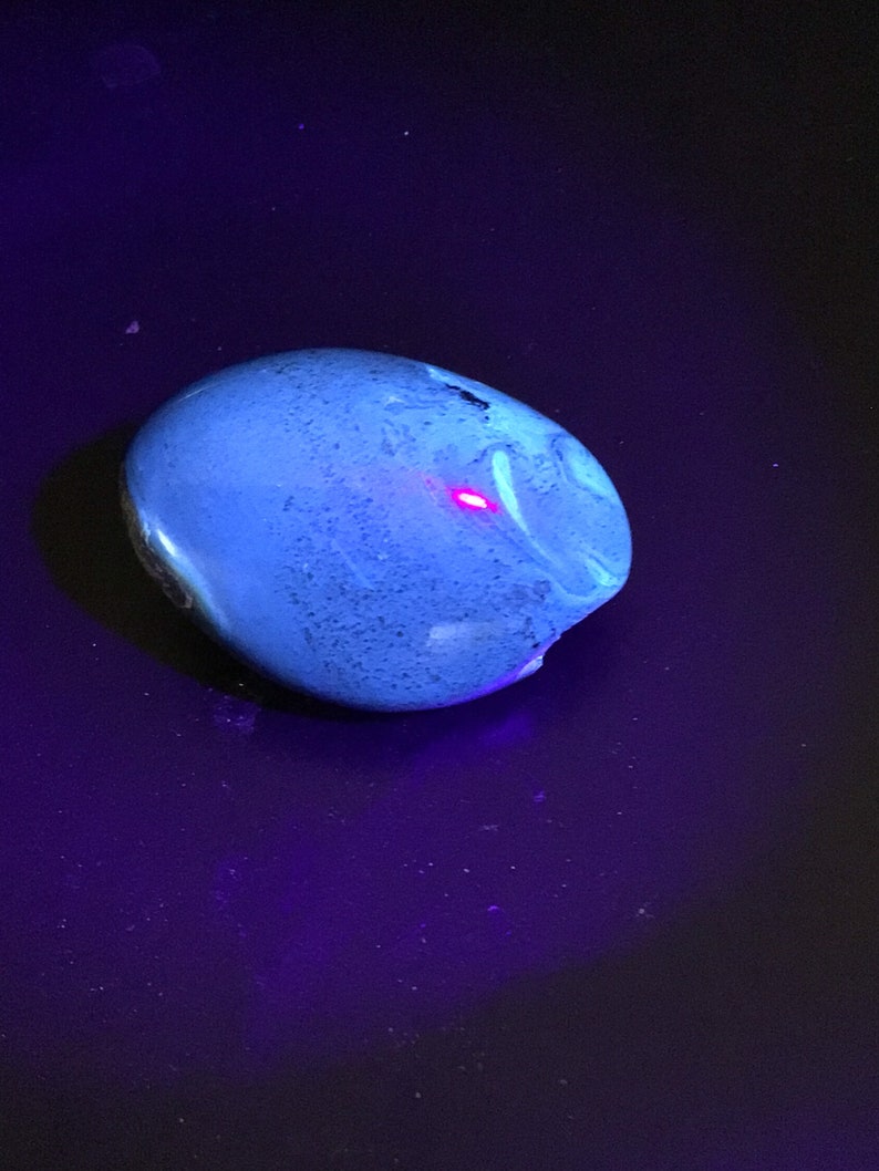 May include: A smooth, blue, oval-shaped stone with a white swirl pattern. The stone is illuminated with a bright, pink light.