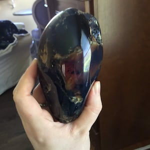 May include: A large, dark amber stone with a unique, swirling pattern of brown, black, and purple hues. The stone is smooth and polished, with a glossy finish.