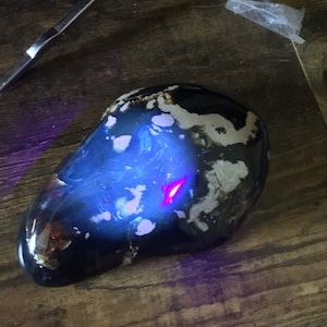 May include: A dark blue and white agate stone with a swirling pattern. The stone is illuminated with a purple light, revealing a red streak in the center.