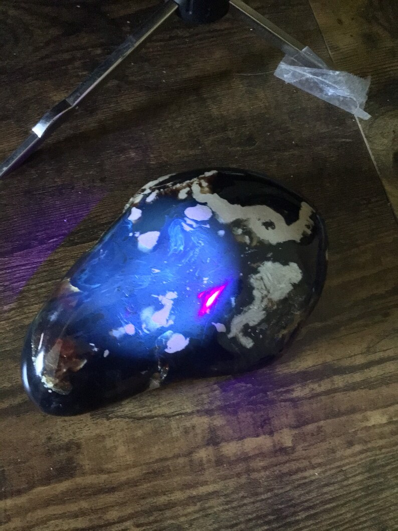 May include: A dark blue and white agate stone with a swirling pattern. The stone is illuminated with a purple light, revealing a red streak in the center.