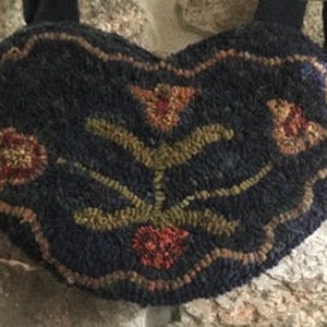 May include: A heart-shaped, dark blue wool rug with a floral design in shades of orange, yellow, and green. The rug has a fringe border and is attached to a black strap.