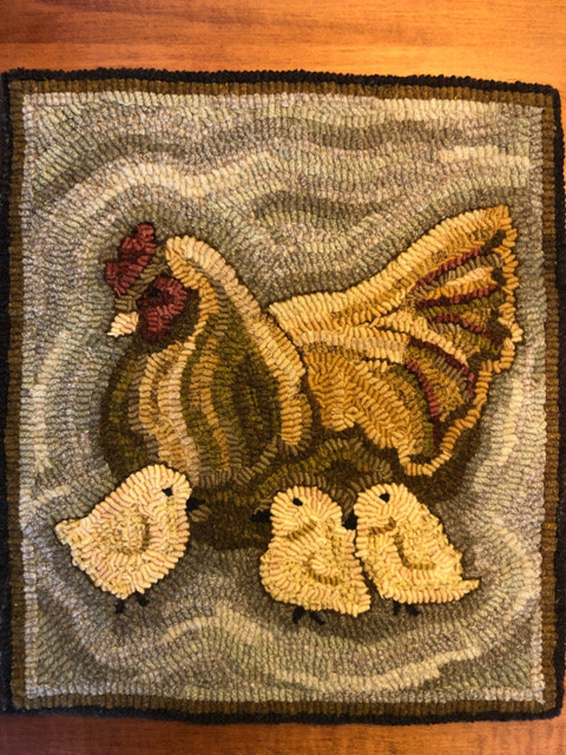 Puede incluir: Una alfombra hecha a mano que representa una gallina marr&oacute;n y amarilla con tres pollitos amarillos. La gallina est&aacute; de pie sobre un fondo azul claro con un patr&oacute;n ondulado.