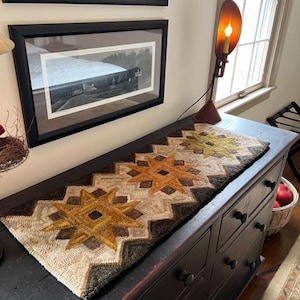 May include: A brown wooden dresser with six drawers and black knobs. A woven rug with a geometric pattern in shades of brown, beige, and orange is placed on top of the dresser.