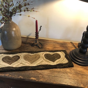 May include: A brown wooden table with a brown and white heart-shaped rug, a ceramic vase with green and red flowers, a black candle holder with a red candle, and a black lamp with a white shade.