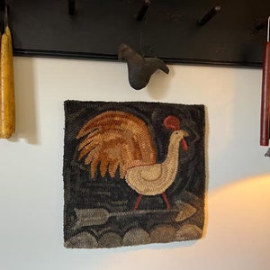 May include: A rooster-themed wall hanging with a black background and a beige and brown rooster design. The image also shows two yellow candles, two burgundy candles, and a black wall rack.