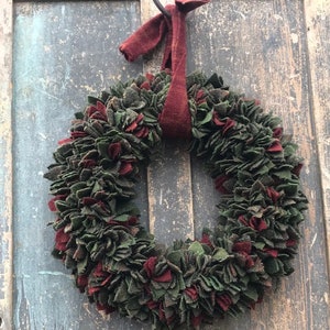 May include: A green and red felt Christmas wreath with a red felt ribbon hanging on a rustic wooden door.