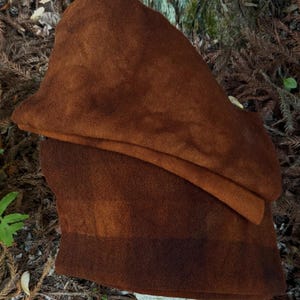 May include: A brown medieval-style hood made of a soft, textured fabric. The hood features a deep, pointed cowl and a wide brim, offering protection from the elements. The color is a rich, earthy brown, with a slightly darker band at the base.