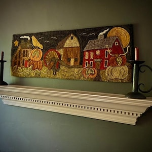 May include: A colorful wool rug depicting a rural scene with three houses, a bird, and pumpkins. The rug is hanging on a white mantel above a fireplace.