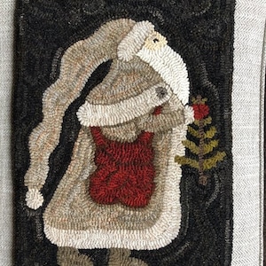 May include: A hand-stitched wool rug depicting a whimsical Santa Claus figure in a white suit, carrying a red bag and a green tree. The rug has a black background and a white border.