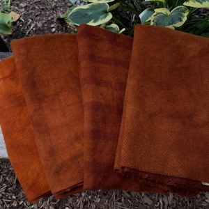 May include: Four folded pieces of fabric in varying shades of burnt orange and rust. Each piece features a distinct, fine-textured weave pattern, displaying a consistent color palette ranging from lighter terracotta to deeper, darker brown-orange tones.