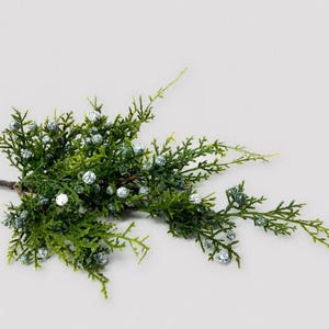 May include: A sprig of artificial greenery with small, round, silver-speckled berries. The evergreen branches are a vibrant green, creating a natural and festive appearance. Ideal for holiday decorations or craft projects.