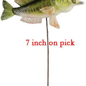 May include: A decorative fish on a pick, approximately 7 inches (17.78 cm) long. The fish has green, yellow, and orange coloring with an open mouth. The text "7 inch on pick" is printed in red.