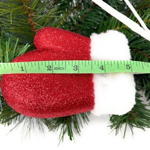 One of the red glittered mittens from the floral spray on a Christmas pine background with a ruler showing length of 5".