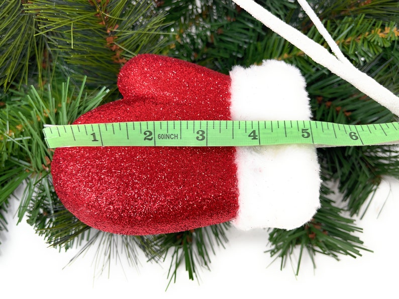 One of the red glittered mittens from the floral spray on a Christmas pine background with a ruler showing length of 5".