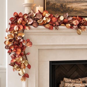 May include: A decorative garland featuring metallic-finished leaves in shades of red, copper, bronze, and gold, interspersed with small clusters of dark berries. The garland is draped over the edge of a fireplace mantel, cascading down one side.