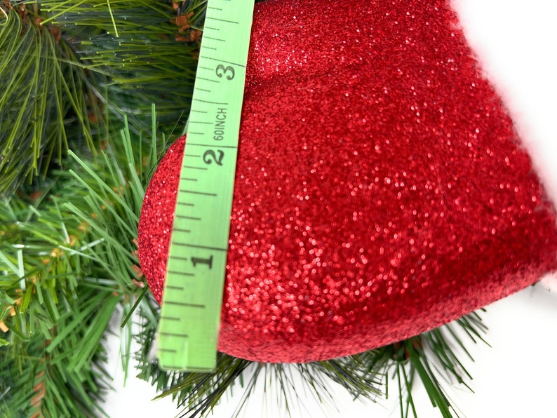 One of the red glittered mittens from the floral spray on a Christmas pine background with a ruler showing width of 4".
