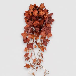 May include: A hanging artificial plant featuring a dense cluster of maple-shaped leaves in various shades of deep red, burnt orange, and brown. The foliage is attached to thin, flexible brown stems that cascade downward in a natural, trailing arrangement.
