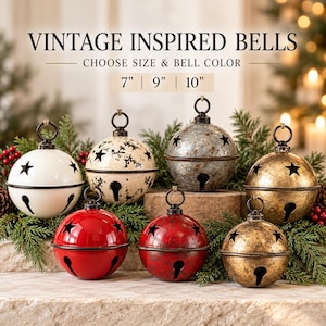 May include: A collection of round metal jingle bells featuring star-shaped cutouts and a top hanging loop. The bells come in various finishes including solid white, speckled cream, distressed silver, red, and gold. Text reads VINTAGE INSPIRED BELLS 7" | 9" | 10".