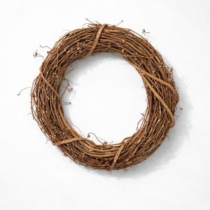 May include: A circular wreath made of intertwined brown twigs. The wreath is a natural brown color and has a rustic appearance. The twigs are tightly woven together, creating a full and textured look. This wreath is suitable for seasonal home decor.