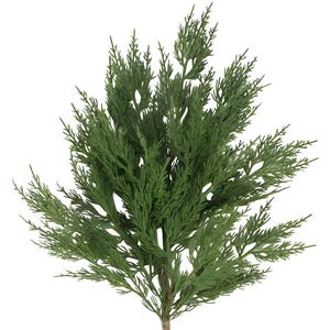 May include: A close-up of a green artificial cedar branch. The branch has many small, needle-like leaves and a brown stem. The leaves are a vibrant green color, and the branch is set against a white background.