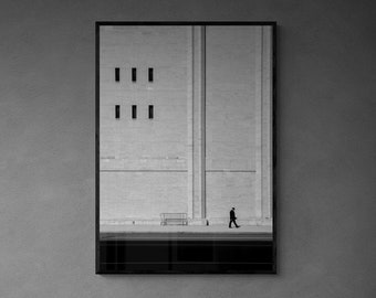 May include: A black and white photograph of a building with three windows hangs on a grey wall above a fireplace. The fireplace has a black surround and a fire burning inside. There are three decorative items on the mantelpiece, including a white coral sculpture, a black plant, and a white ceramic vase.