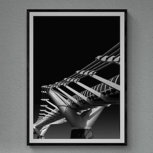 Puede incluir: Una fotografía en blanco y negro de un puente con una estructura metálica. La foto está enmarcada en un marco negro y está colgada en una pared gris.
