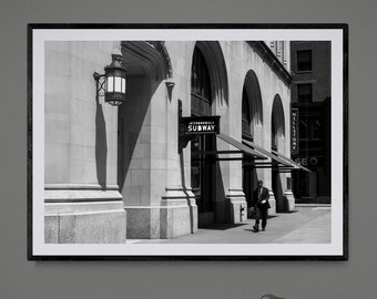 May include: Black and white framed photograph of a city street scene. A person walks past a building with arched windows and a sign that reads "SUBWAY". A vintage radio sits on a white surface below the framed photo.
