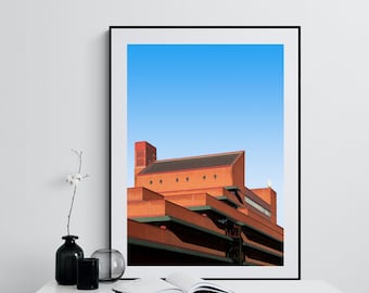 May include: A framed photograph of a modern, red brick building with a blue sky in the background. The building has a layered design with multiple levels and windows.