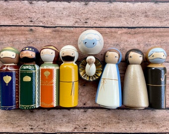 May include: A set of wooden peg dolls depicting the Nativity scene. The dolls are painted in various colors, including blue, green, yellow, orange, and brown. The set includes Mary, Joseph, the baby Jesus, a sheep, and three wise men.