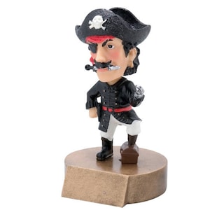 May include: A black and white figurine of a pirate with a red bandana, an eyepatch, and a black hat with a skull and crossbones. The pirate is holding a sword and a treasure chest. The figurine is standing on a gold-colored base.